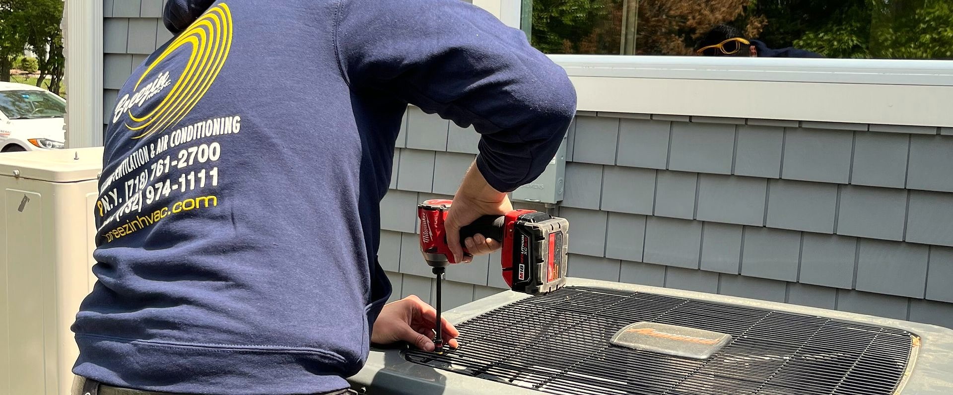 Technician in Breezin sweatshirt drilling on outdoor AC condenser unit